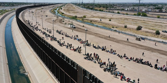 Migrants wait along border wall